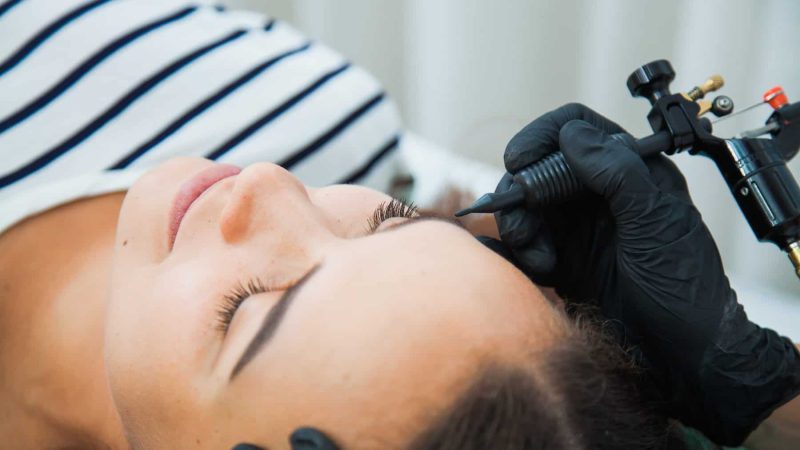Young woman on permanent make-up procedure, tattooing eyebrows in natural tint. Eyebrow Correction closeup. Beauty Concept.