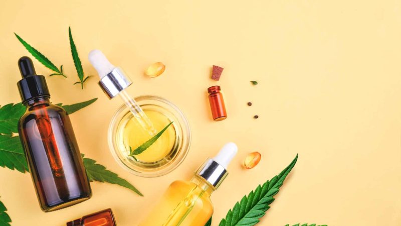 Different glass bottles with CBD OIL, THC tincture and cannabis leaves on yellow background. Flat lay, minimalism. Cosmetics CBD oil.