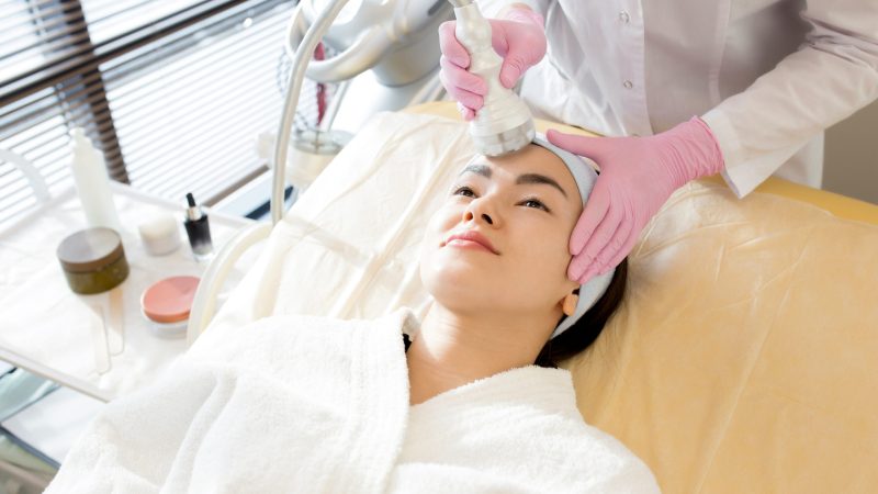 High angle portrait of pretty Asian woman enjoying facial care in cosmetologist office, copy space