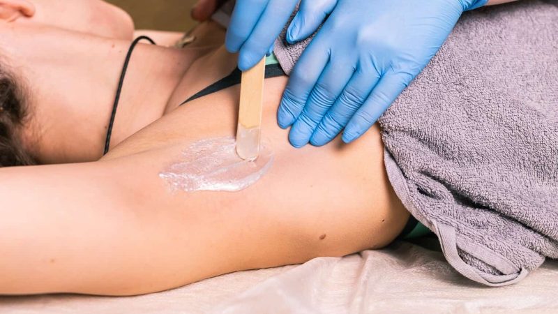 Waxing woman armpit with spatula. Salon wax beautician epilation procedure. Waxing female body for hair removal by therapist close up. Smooth underarm concept.