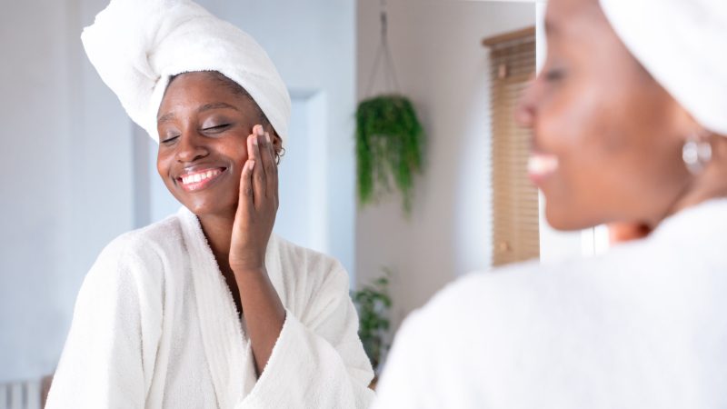 Skincare, face and cosmetic cream of an African woman using facial beauty products for morning self care. Female with a smile health and wellness in a home bathroom.