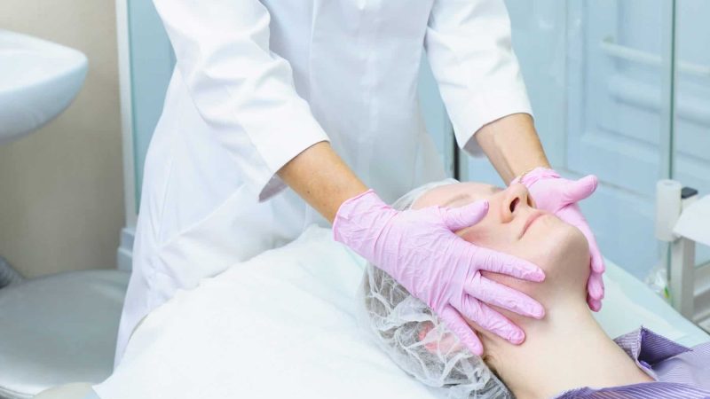 Beautician in pink gloves applies peeling on woman face. Cosmetic procedure for rejuvenation and cleansing of the skin. Spa treatment